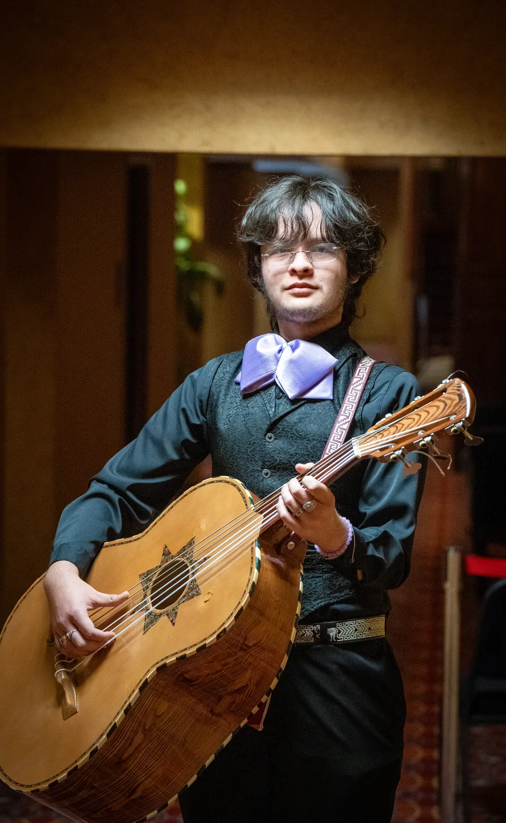 A high school mariachi student holding a guitarrón