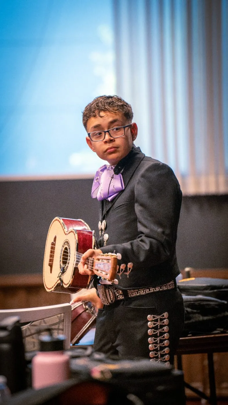 A Harmony Project student with glasses holding a mariachi guitar