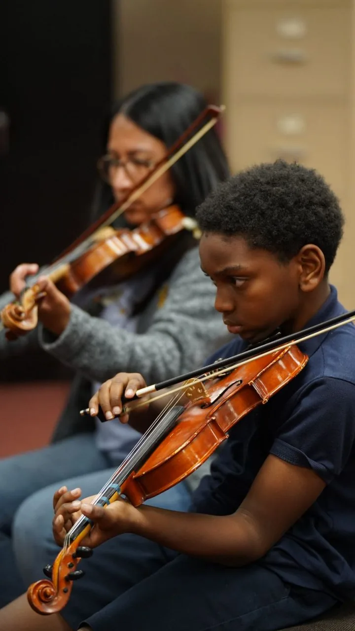 A student plays violin with a teaching artist during a lesson